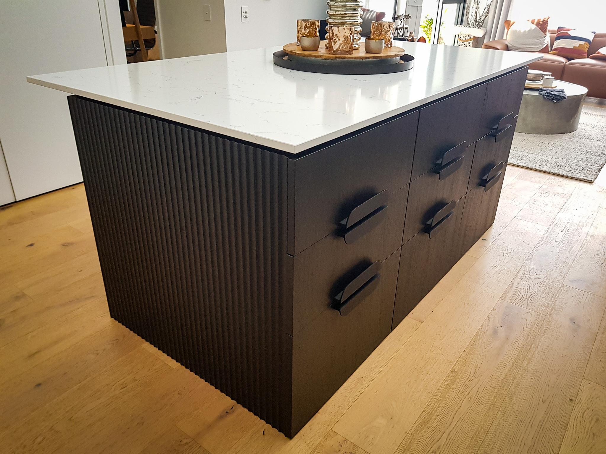 Dark fluted kitchen island with white marble benchtop and black handles